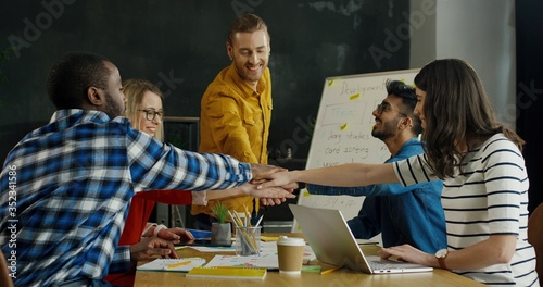 Young mixed-races team of male and female startuppers putting hands on top of each others and doing gesture of friendship. photo