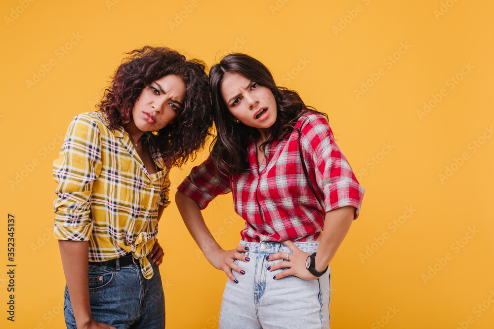 Brown-eyed girls look at camera with outrage and condemnation. Snapshot of disgruntled friends in similar shirts on isolated background Brown-eyed girls look at camera with outrage and condemnation. Snapshot of disgruntled friends in similar shirts on isolated background