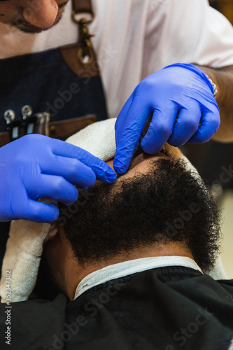 Young Latin Barber At Work In Stylish Barbershop. Cool, bearded man enjoys the moment.