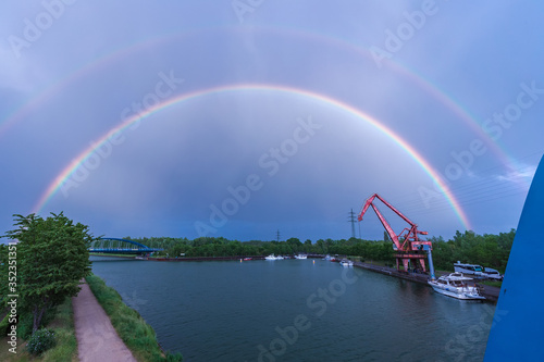 Double beautiful rainbow after rain in the sky above the river and the old crane