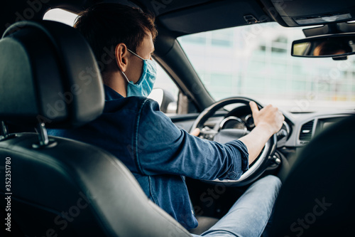 A man in a protective medical mask, sitting behind the wheel of a car. Quarantine, coronavirus