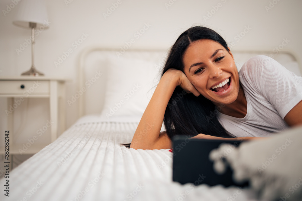 Happy woman having video call over smart phone while lying on bed, close-up, portrait.