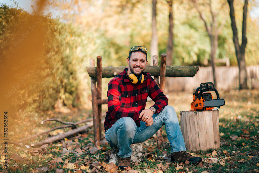 Portrait of a smiling young man cutting wood, preparing for the winter.