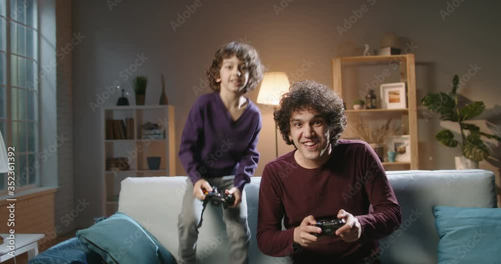 Funny south asian siblings are relaxing together, playing video games in front of tv, father and son expressing emotions while enjoying their hobby - family time concept 4k footage Funny south asian siblings are relaxing together, playing video games in front of tv, father and son expressing emotions while enjoying their hobby - family time concept 4k footage