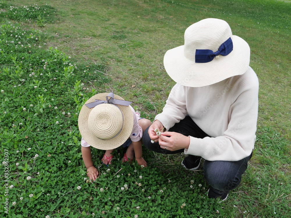 Parent and child picking white clover and their daughter to make a wreath Parent and child picking white clover and their daughter to make a wreath