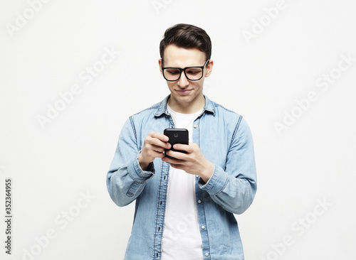 Happy young man in glasses typing sms on white background