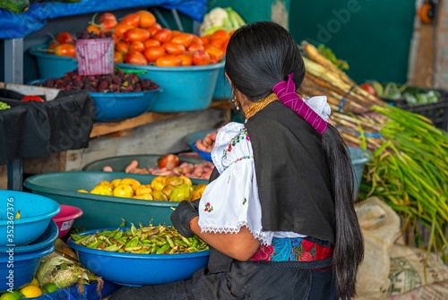 An indigenous Otavalo woman in traditional clothing peeling green beans in the local fruit and vegetable market of Otavalo, Ecuador.