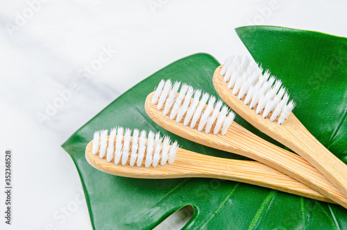 Bamboo toothbrushes with green leaves on marble background.