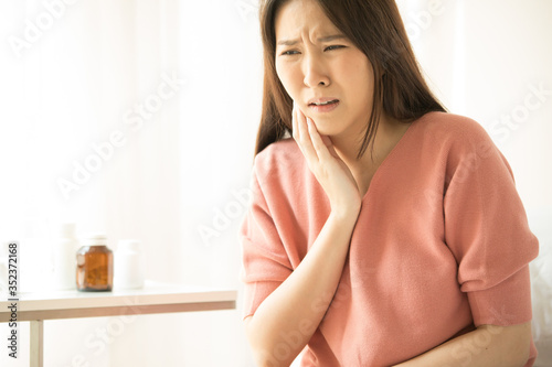 Woman is sitting on bed in her home, she has toothache. concepts of health and medical care