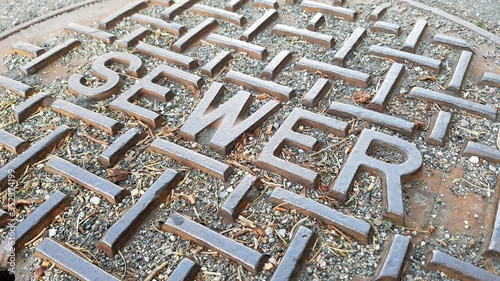 Extreme closeup of metal sewer cap on a dry, cracking road during summer