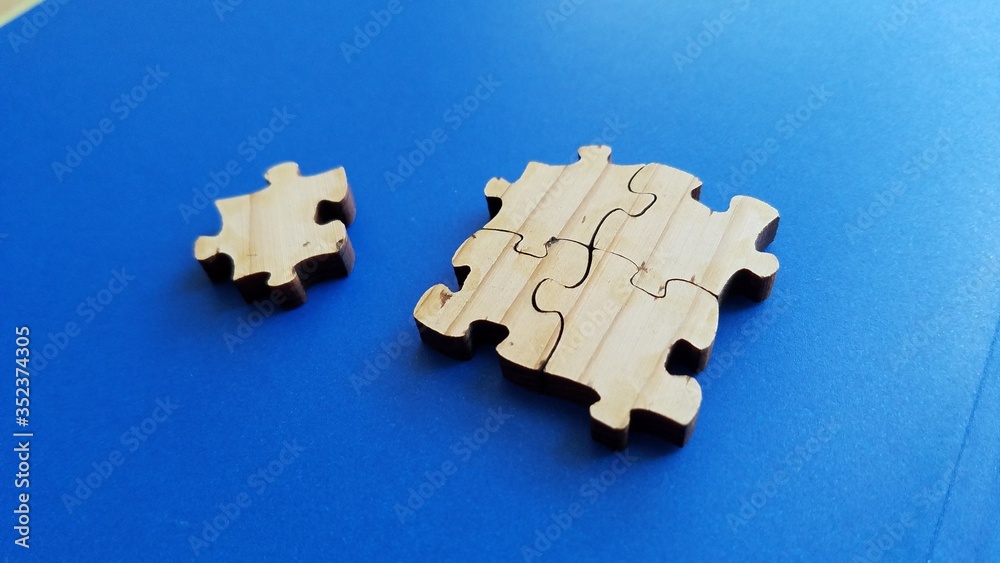 Fototapeta premium Wood surface puzzle pieces close up view on clean blue background, concept of isolation