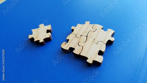 Wood surface puzzle pieces close up view on clean blue background, concept of isolation