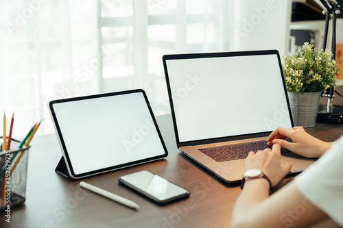 Woman using digital laptop and tablet with smartphone on the table in house. Blank screen for advertising.