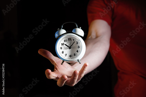 Foto White retro alarm clock hovering above Caucasian male hand against dark backgrou