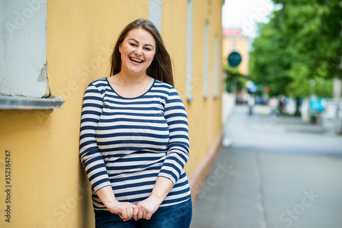 Smiling beautiful woman plus size looking straight into the camera on the street over orange background