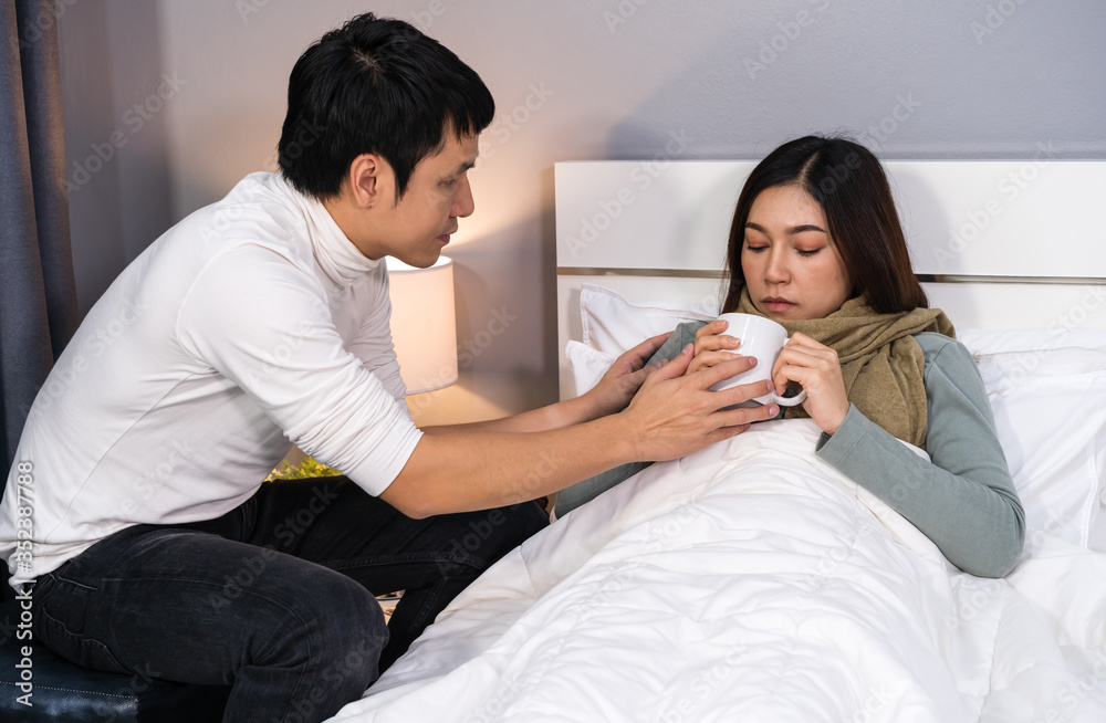 husband bringing a cup of hot water giving his sick wife drinking on bed at home husband bringing a cup of hot water giving his sick wife drinking on bed at home