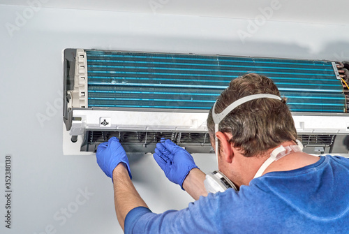 Technician in blue gloves and mask disassembling air conditioner and preparing it for cleaning.