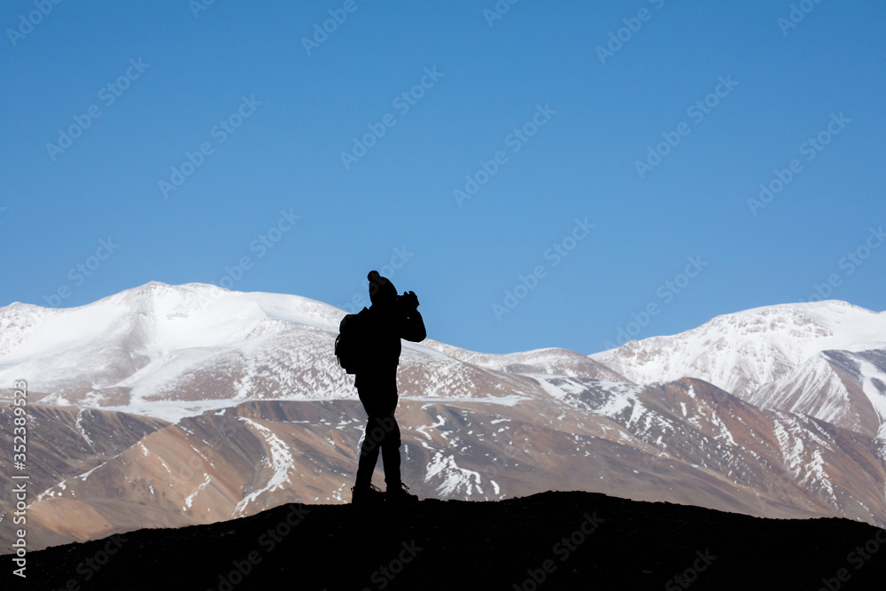 Tourist with backpack taking a photo on the rock in the beautiful mountains view of snowy Tso Moriri Lake in Leh Ladakh india, freedom concept