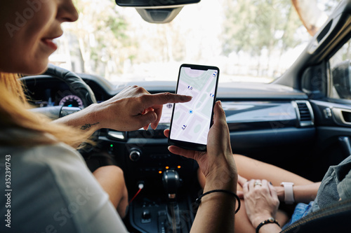 Female friends sitting in car and setting destination point on smartphone application