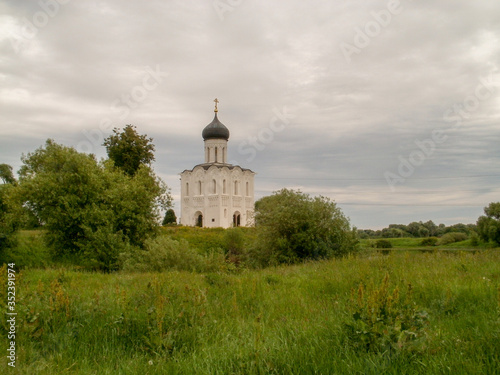 Standing on a hill next to the river among green fields a small one domed old Church