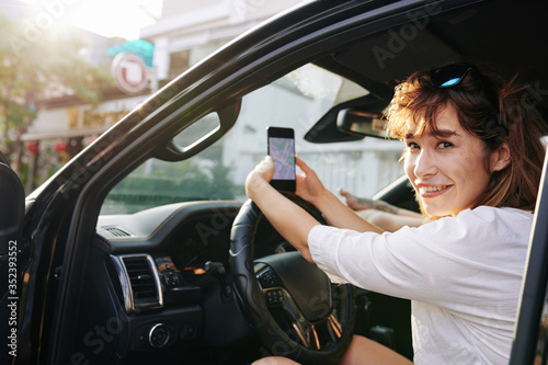 Cheerful pretty young woman using map on smartphone screen when setting destination point