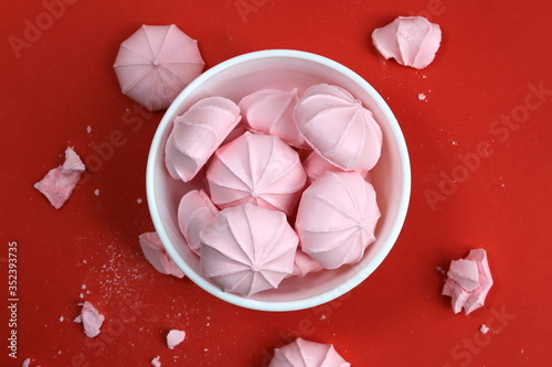 Pink meringue sweets in a white plate on a red background