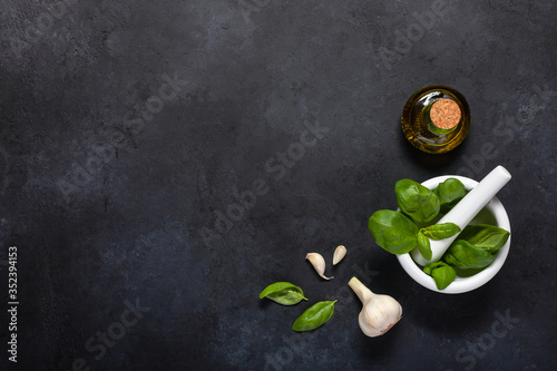 Basil leaves, garlic and olive oil on a black background. Copy space. Top view.