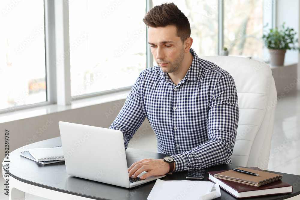 Fototapeta premium Focused young professional man working on laptop in a modern office