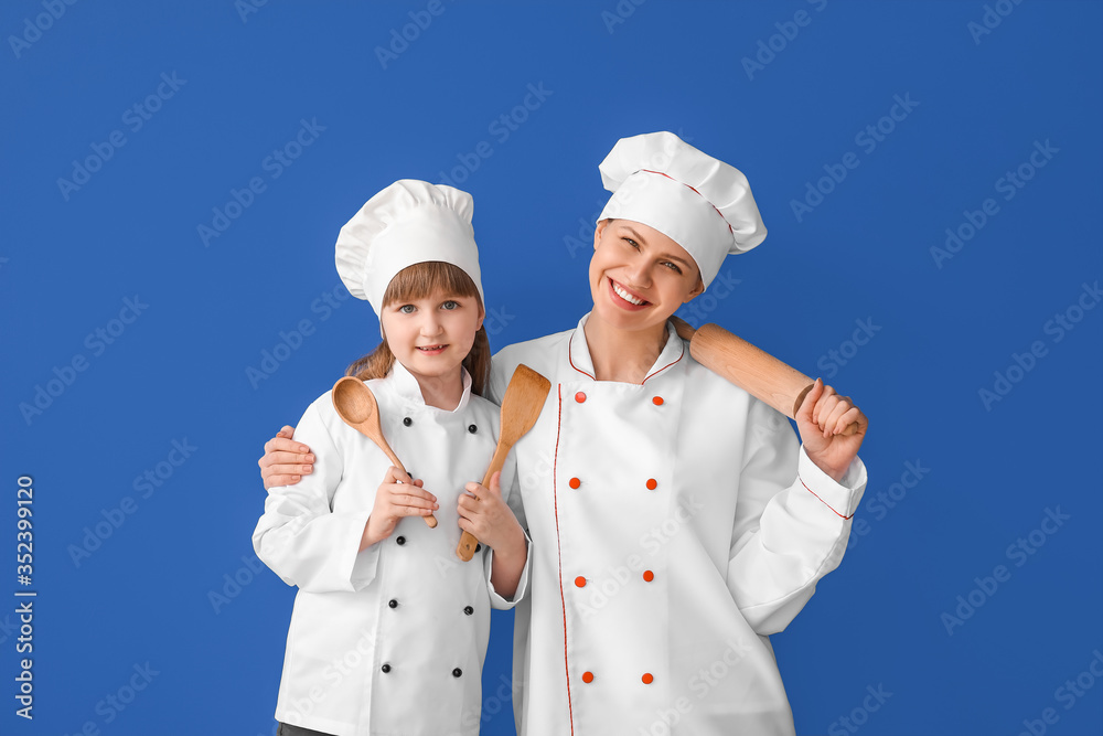 Portrait of female chef and her little daughter on color background Portrait of female chef and her little daughter on color background