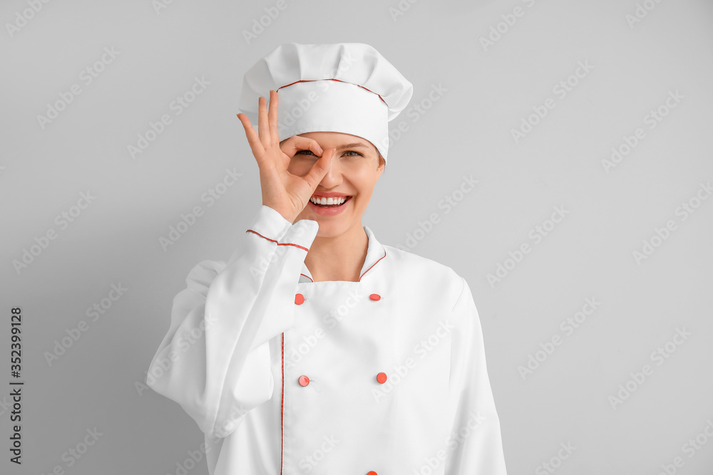 Beautiful female chef showing OK on light background