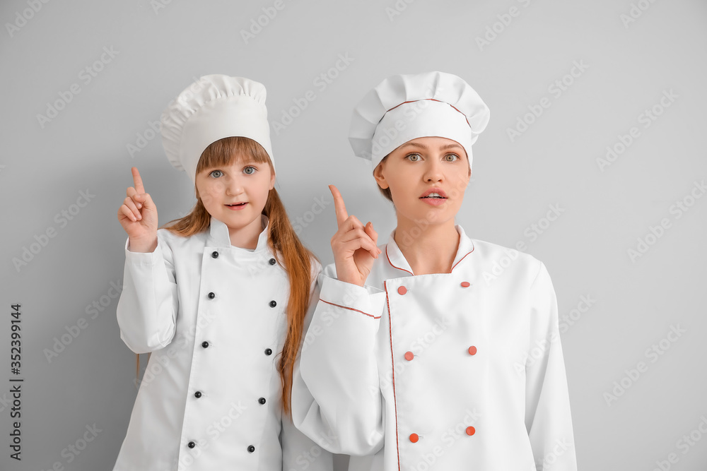 Portrait of female chef and her little daughter with raised index fingers on light background Portrait of female chef and her little daughter with raised index fingers on light background