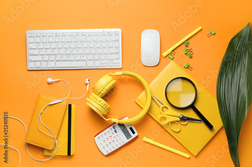 Computer keyboard with stationery and headphones on color background