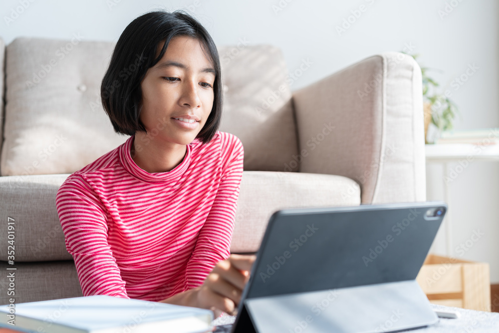 Asian girl is studying online via the internet on tablet while sitting in the living room at sunlight morning, Asia child watching and education distance on the computer. Concept learning at home Asian girl is studying online via the internet on tablet while sitting in the living room at sunlight morning, Asia child watching and education distance on the computer. Concept learning at home