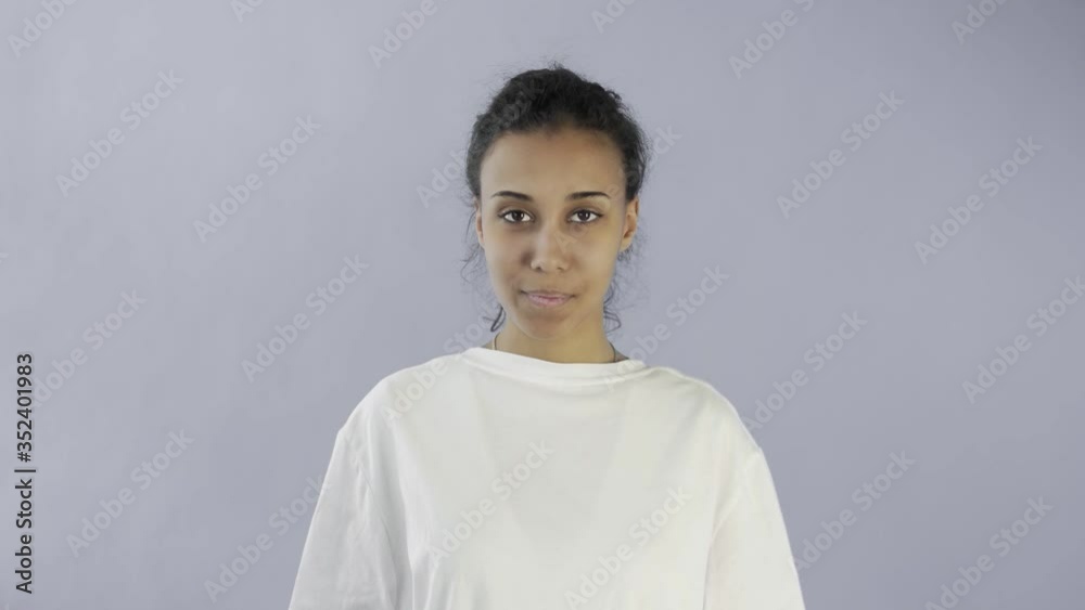 CuteAfro-American Girl is showing ok with two thumbs and smiling on grey Background in Studio