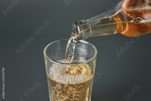 Pouring of apple cider into glass on grey background