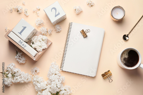Composition with beautiful lilac flowers, calendar, notebook and coffee on color background