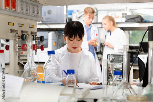 Portrait of Asian female scientist registering results of research in notebook at biochemical laboratory