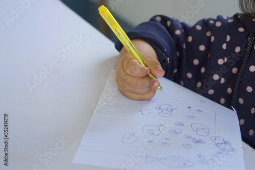 ,Childhood with muscle practice and brain development concept. Close up hand ofasian three year olds a little girl using a pen to scratch a line on book in emotion of attention. photo