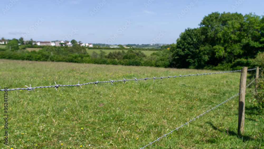 Barbed wire fence views in to farm fields with small village in the distance