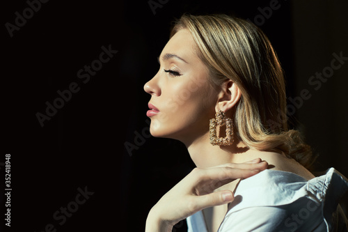 Blonde women with jewelry earrings in their ears in the rays of the evening sun. Beauty face long hair clean smooth skin, natural cosmetics and makeup