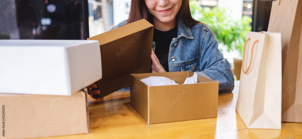 A beautiful young asian woman receiving and opening a postal parcel box and shopping bags at home for delivery and online shopping concept A beautiful young asian woman receiving and opening a postal parcel box and shopping bags at home for delivery and online shopping concept