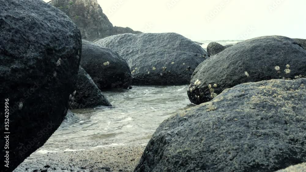 Sea water getting between rocks reaching the sand on the shore of a beach with the ocean and a mountain background close up shot Sea water getting between rocks reaching the sand on the shore of a beach with the ocean and a mountain background close up shot