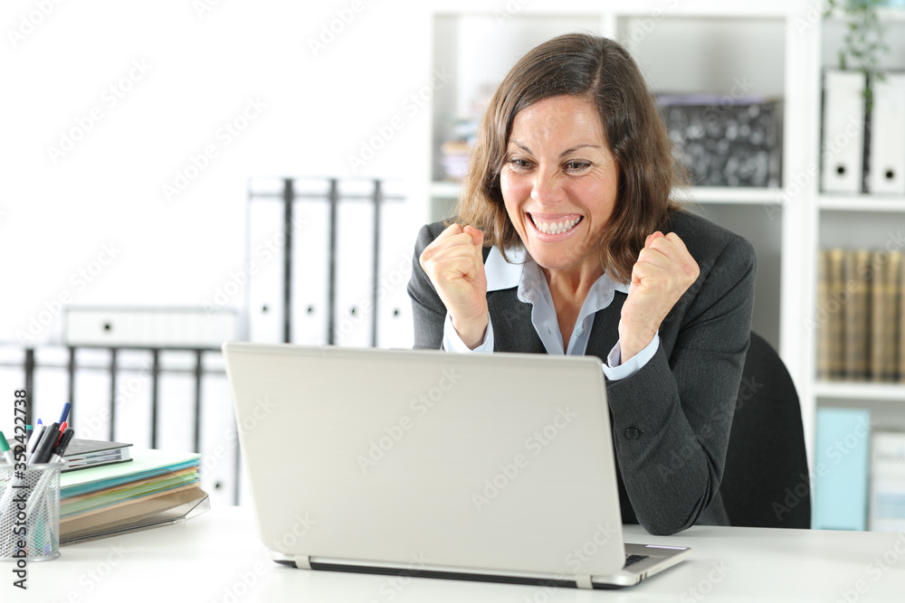 Excited adult executive celebrating news on laptop at office Excited adult executive celebrating news on laptop at office