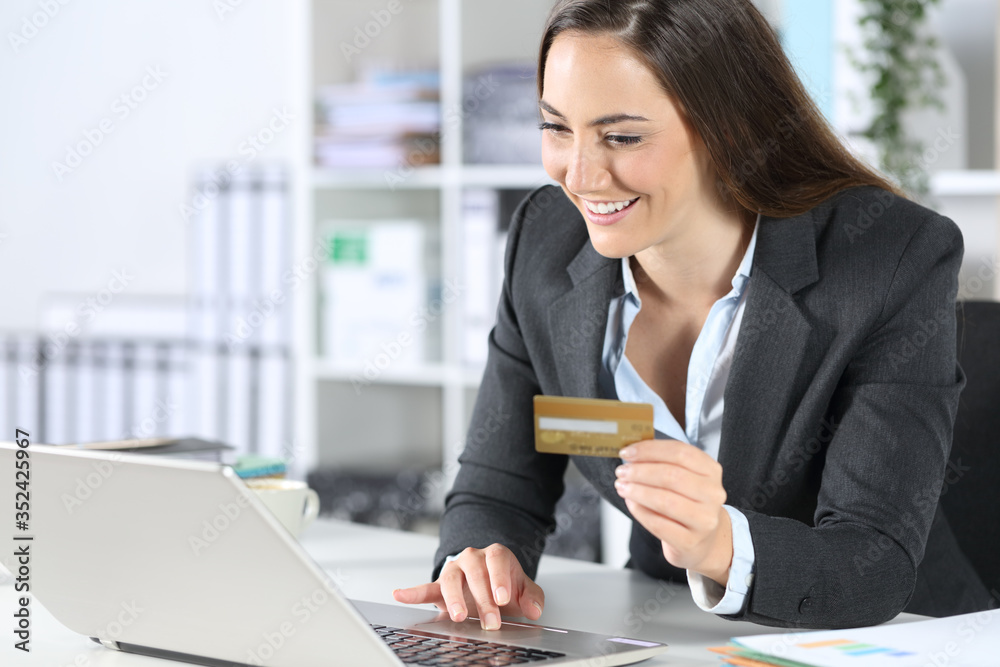 Happy executive pays online with card on laptop at office Happy executive pays online with card on laptop at office