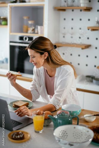 Beautiful woman eating breakfast in the kitchen. Young woman reading the news online. 