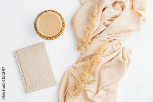 Flat lay autumn composition. Top view beige blanket, cup of coffee, paper notebook and dry flowers on white table. Cozy home office desk, boho style.