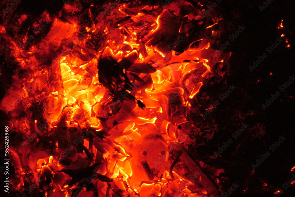 The fire charcoals of a bonfire glow in the night with red heat. Abstract dark and red-orange background. The fire charcoals of a bonfire glow in the night with red heat. Abstract dark and red-orange background.