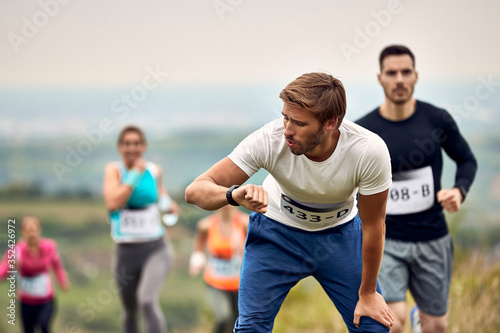 Athletic man checking his heart rate on smart watch after running marathon in nature.