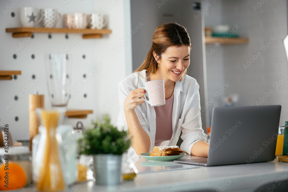 Beautiful woman eating breakfast in the kitchen. Young woman reading the news online. Beautiful woman eating breakfast in the kitchen. Young woman reading the news online.