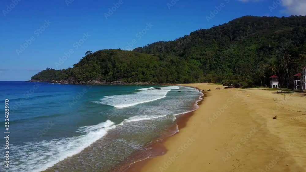 Steady aerial drone flight shortly panning over waves crashing at colorful empty deserted paradise beach Tioman Island Malaysia. Yellow sand with forest, palm trees and mountains in the background. Steady aerial drone flight shortly panning over waves crashing at colorful empty deserted paradise beach Tioman Island Malaysia. Yellow sand with forest, palm trees and mountains in the background.